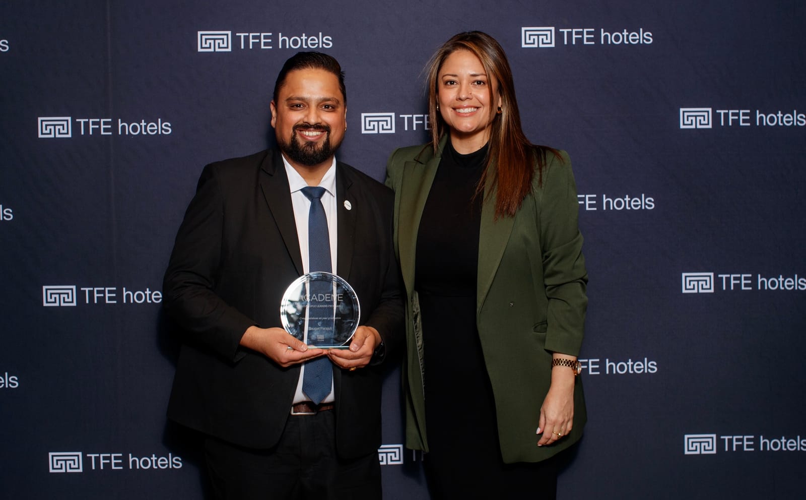 Two colleagues holding an award in front of a TFE Hotels backdrop at the TFE Awards