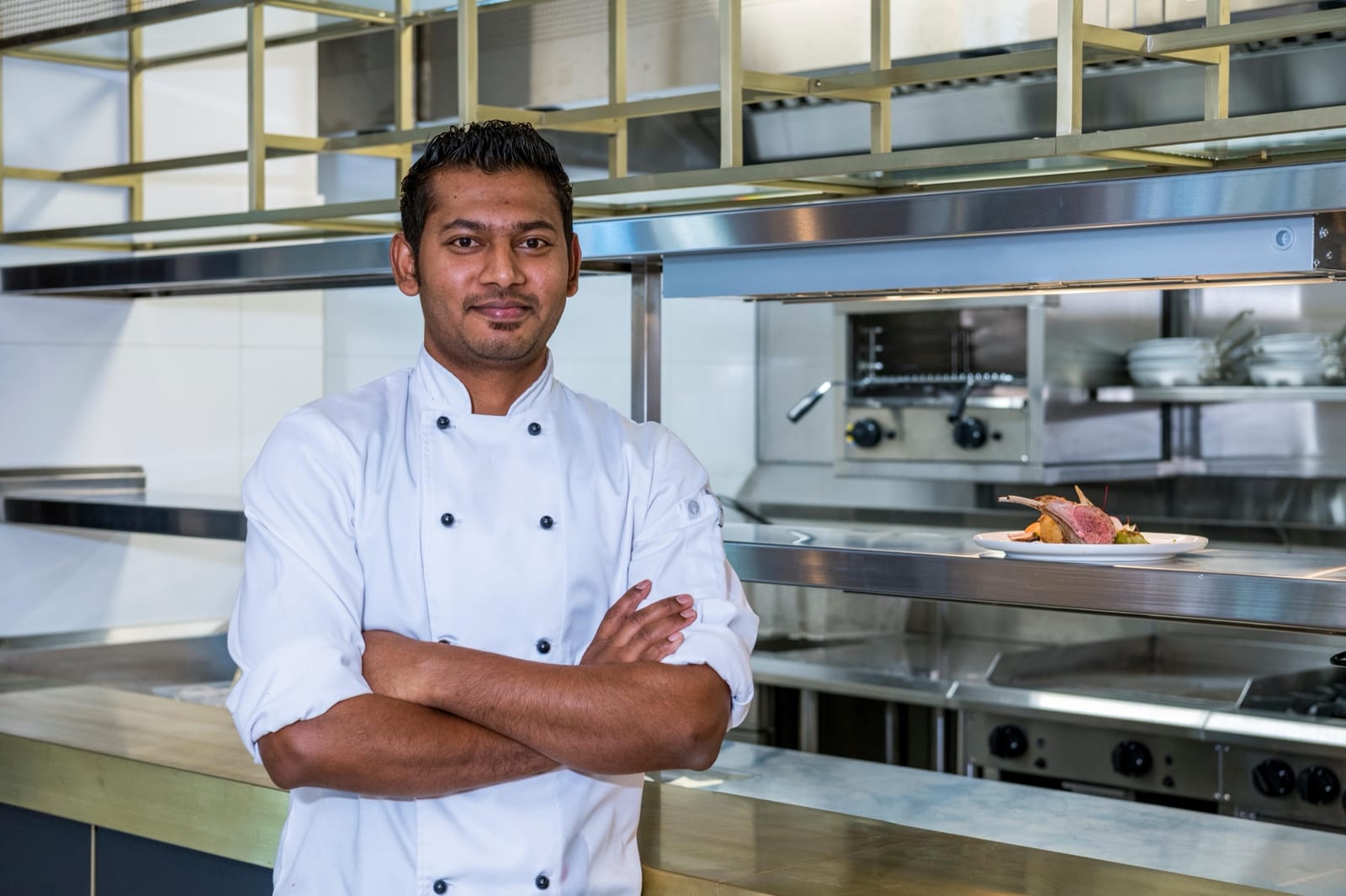 A chef standing with arms folded in the kitchen at Vibe Hotel Melbourne